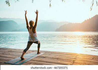 Beautiful woman practicing Yoga by the lake - Sun salutation series - Virabhadrasana - Toned image