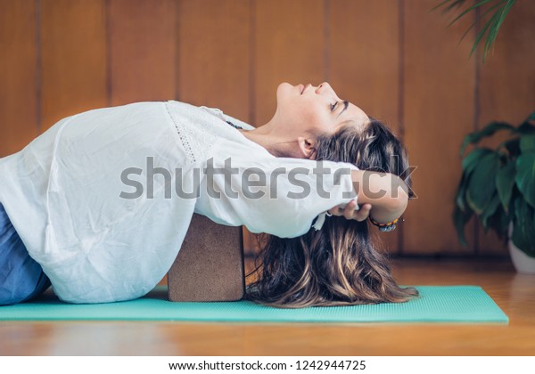 Beautiful woman practicing yoga using\
yoga blocks at home. Lying on back on turquoise yoga\
mat.