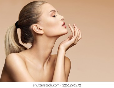 Beautiful woman in profile touching her lips. Photo of woman finishes makeup on beige background. Youth and skin care concept