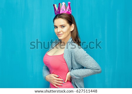 Beautiful woman is proud her big breast. Isolated portrait of girl with paper crown, blue wall back.