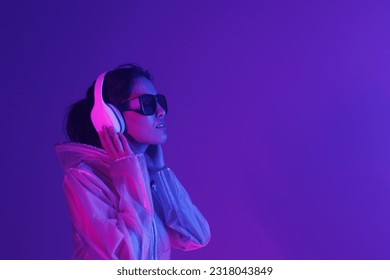 Beautiful woman with purple hair in futuristic costume over dark background. Violet neon light. Portrait of young girl in modern headphones listening music. - Shutterstock ID 2318043849
