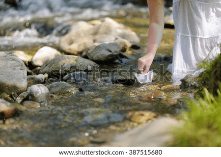 A beautiful woman is putting paper boat on the water