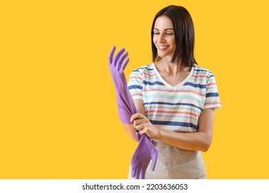 Beautiful Woman Putting Rubber Glove On Yellow Background