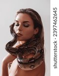 Beautiful woman with python snake elegantly slithering over her neck.