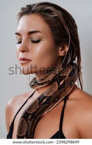 Beautiful woman with python snake elegantly slithering over her neck.