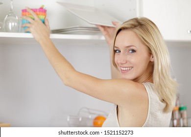 beautiful woman reaching for crockery from kitchen cupboard