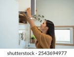 Beautiful woman reaching for ingredients in upper kitchen cabinets