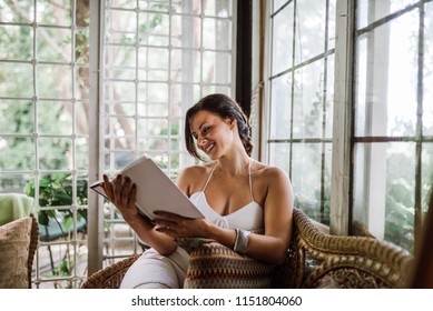 Beautiful Woman Reading A Book In A Sunroom Or Conservatory Extending Into The Garden.