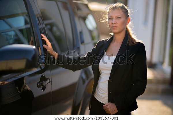 Beautiful woman real estate agent in suit and\
black car on the background of the\
house