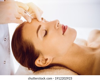 Beautiful woman receiving beauty injections with closed eyes in sunny medical center. Beautician doctor hands doing beauty procedure to female face with syringe. Cosmetic medicine and surgery concept - Powered by Shutterstock