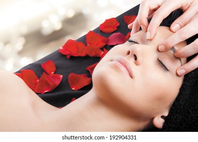 Beautiful Woman Receiving A Facial Massage Lying On Bed With Rose Petals.