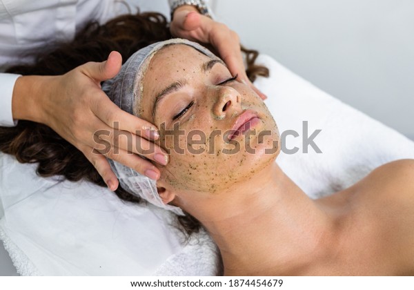 Beautiful woman receiving\
natural green peel facial mask with rejuvenating effects in spa\
beauty salon.