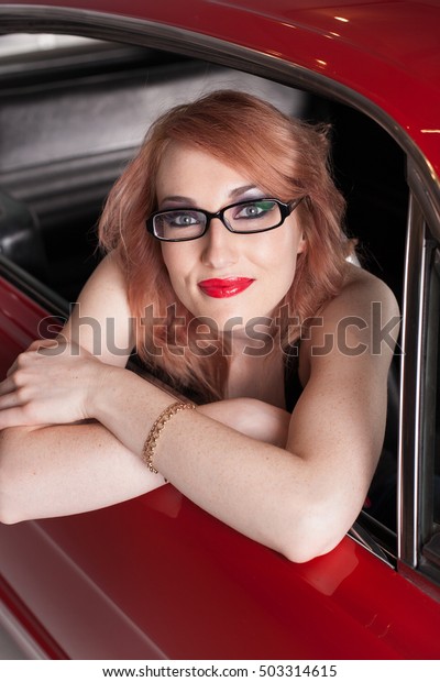 Beautiful Woman with Red hair and wearing black rim\
glasses in Red car