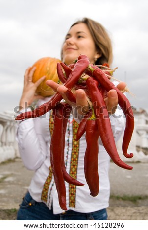 beautiful woman with red hot pepper and pumpkin during celebration of Halloween. Soft-focused. Focus is on pepper