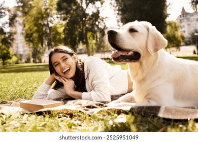 A beautiful woman relaxes on a blanket in the park, smiling while her dog lies beside her. - Powered by Shutterstock