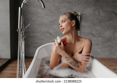 Beautiful Woman Relaxing In Bathtub And Looking At Window, Calm Young Lady Sitting In Hot Bath, Resting In Modern Bathroom Interior, Enjoying Domestic Spa, Copy Space