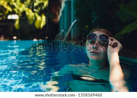Beautiful Woman Relaxing In Swimming Pool Water. Girl With Healthy Tanned Skin, Gorgeous Face, And Wet Hair Enjoying Summer Sun On Hot Summer Day At Pool Edge At Luxury Resort.