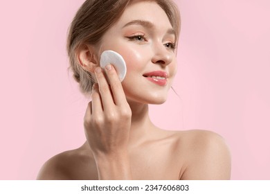 Beautiful woman removes make-up and cleanses her skin with cotton pads on a pink background