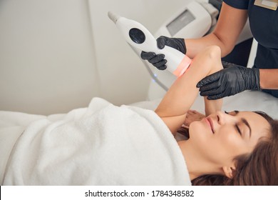 Beautiful woman resting while getting slimming procedure at beauty salon with help of cavitation device