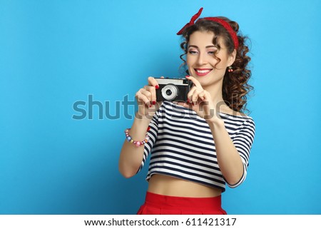 Beautiful woman with retro camera, wearing pin-up style, posing in studio on blue background;