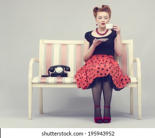 Beautiful woman in retro style drinks coffee sitting on the couch.