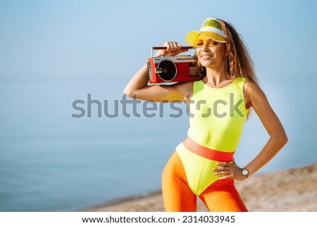Beautiful woman with retro tape record player enjoying a summer day on the beach. Сoncept of sports, fitness, aerobics. Active sport.