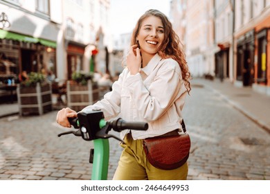 Beautiful woman rides an electric scooter in the city street on a sunny day. Ecological transport. Active lifestyle. - Powered by Shutterstock