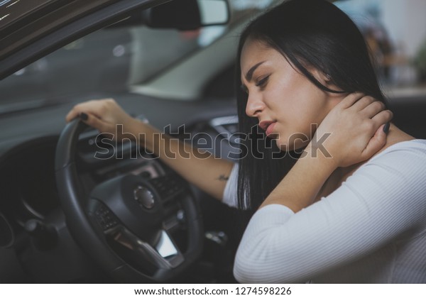 Beautiful woman rubbing her neck, feeling sore\
after long drive. Female driver having neck pain after whiplash\
injury in car crash. Woman suffering from back pain. Healthcare,\
safety, pain concept