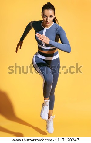 Beautiful woman runner in silhouette on yellow background. Photo of sporty woman in fashionable sportswear. Dynamic movement. Strength and motivation. Full length