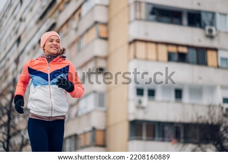 Beautiful woman running on a city street with snow on cold winter day. Sport, fitness inspiration and motivation. Jogging during a bad and extreme weather, during a winter and snow. Copy space.