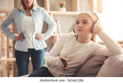 Beautiful woman is scolding her teenage daughter, girl is listening to music in headphones and ignoring her mom