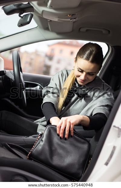 Beautiful woman searching through her bag. Woman\
driver making a stop at the red light. Going through her bag. Young\
blonde woman sitting in her\
car.