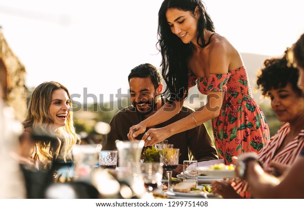 Beautiful woman\
serving food to friends sitting at dinner table. Group of friends\
having a party together\
outdoors.