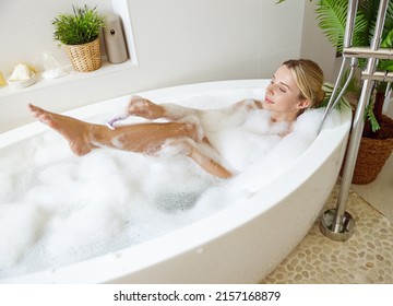 Beautiful woman shaving leg with razor in bathtub with foam. Relaxation and taking care. - Shutterstock ID 2157168879