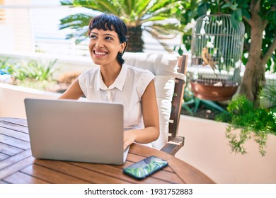Beautiful woman with short hair sitting at the terrace on a sunny day working from home using laptop
