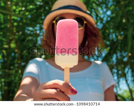Beautiful Woman Short Hair Wearing White Shirt, Beach Hat and Round Sunglasses Holding White and Pink Frozen Popsicle Ice Pop on Summer Time with Sunshine on Tree and Blue Sky Background