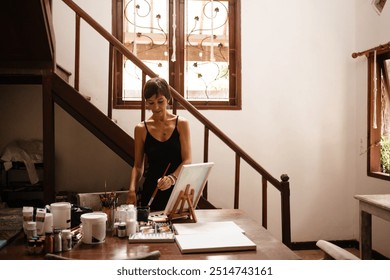 Beautiful woman with short haircut in her art studio. The artist draws a picture at a large wooden table. The concept of creativity and self-care - Powered by Shutterstock