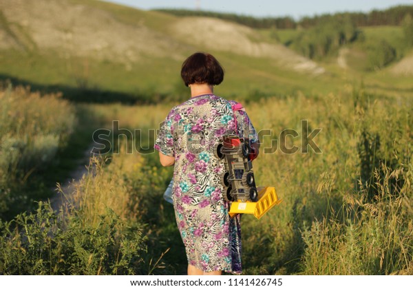 A beautiful woman with a short haircut and a toy\
car over her shoulder is walking along the path towards the hills.\
A woman free from vanity enjoys nature and clean air. Mom with a\
toy meets her child