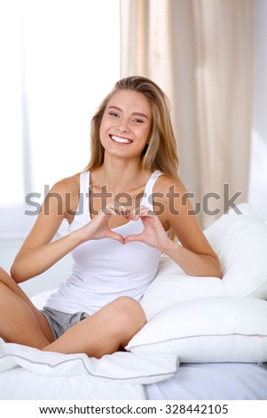 Beautiful woman showing heart shape on her hand , sitting bed