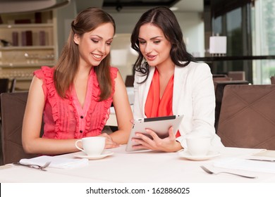 Beautiful Woman Showing Her Friend Photos On Tablet. Sharing Memories From The Trip Or Event 