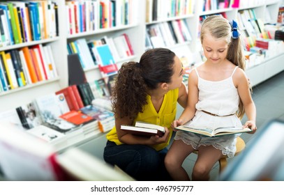 Beautiful Woman Showing Open Book To Girl In School Age In Book Boutique. Focus On The Woman