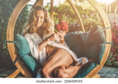 beautiful woman sits on a wooden swing with a bouquet of red roses in her hand. - Shutterstock ID 2206509193