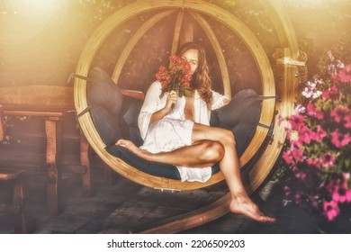 beautiful woman sits on a wooden swing with a bouquet of red roses in her hand. - Shutterstock ID 2206509203