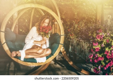beautiful woman sits on a wooden swing with a bouquet of red roses in her hand. - Shutterstock ID 2206509205
