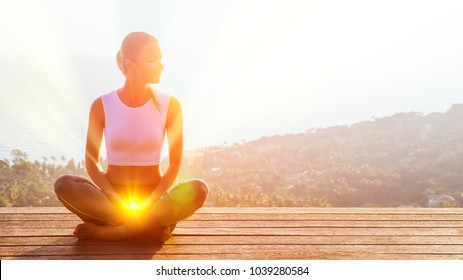 Beautiful woman sits in a pose of a half lotus on high place amazing view of the island outside, she practicing yoga meditation glowing the second sacral chakra eyes closed calm. Kundalini energy