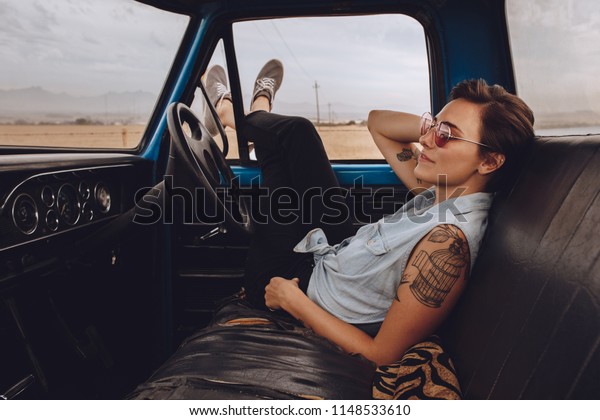 Beautiful\
woman sitting in a car and resting with legs outside window. Woman\
taking break driving a truck on road\
trip.