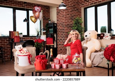 Beautiful Woman Sitting In Living Room Filled With Valentines Day Expensive Gifts, Girl With Luxury Wrapped Present Boxes, Bear Soft Toy, Roses, Balloons. February 14 Romantic Surprises