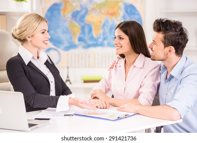Beautiful woman sitting at office with clients and proposing hot tours to them.