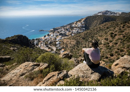 Beautiful woman sitting on a cliff with the mediterranean sea and small coast town in the background in Spain
