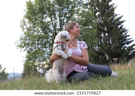 Beautiful woman sitting on the meadow in the park with her dog.
Pets and nature lover.